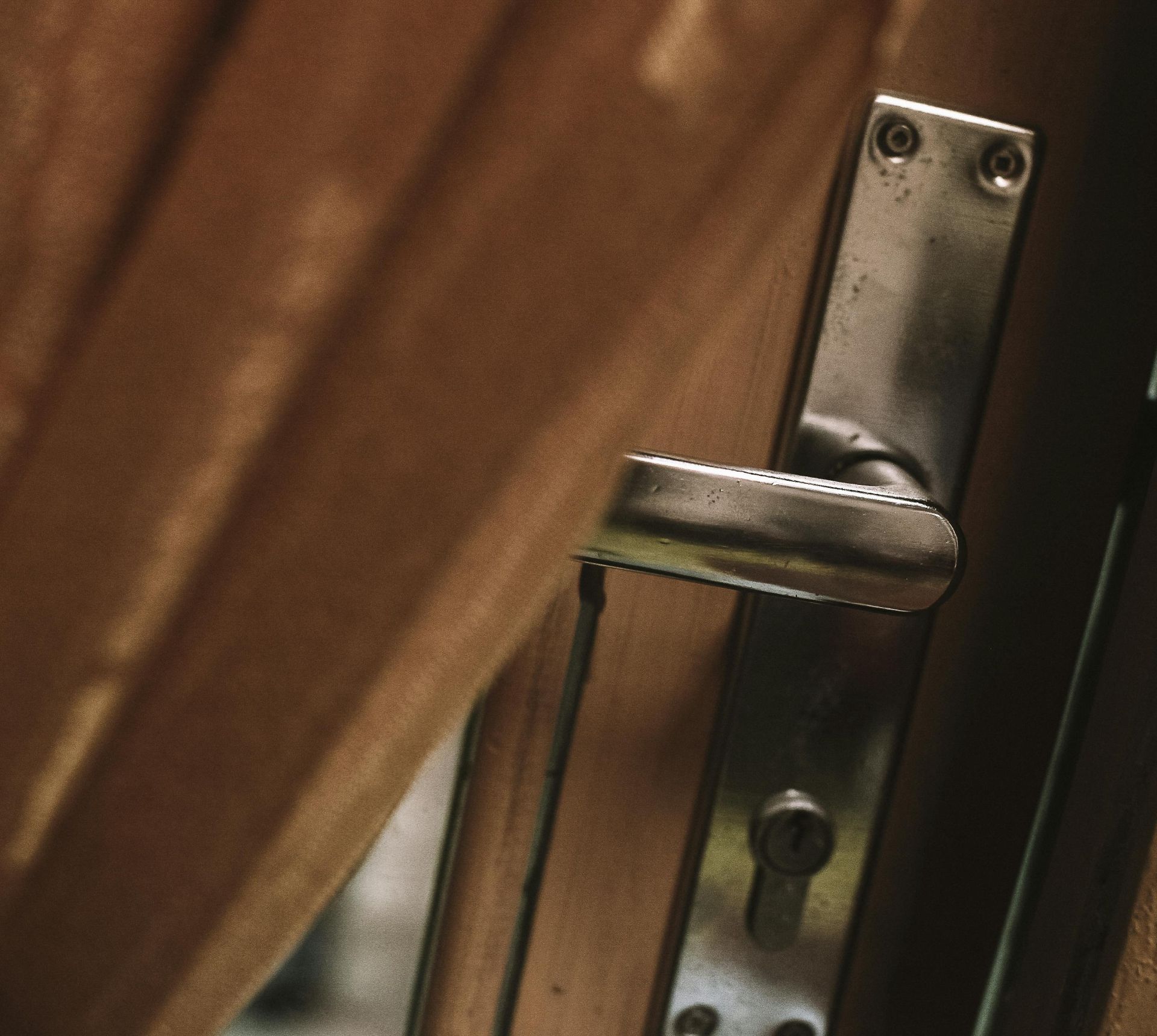 A metal door handle slightly ajar against a wooden background.